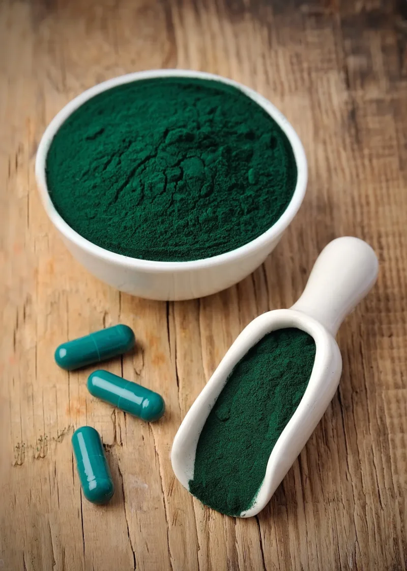 Spirulina powder and green capsules on a wooden table.