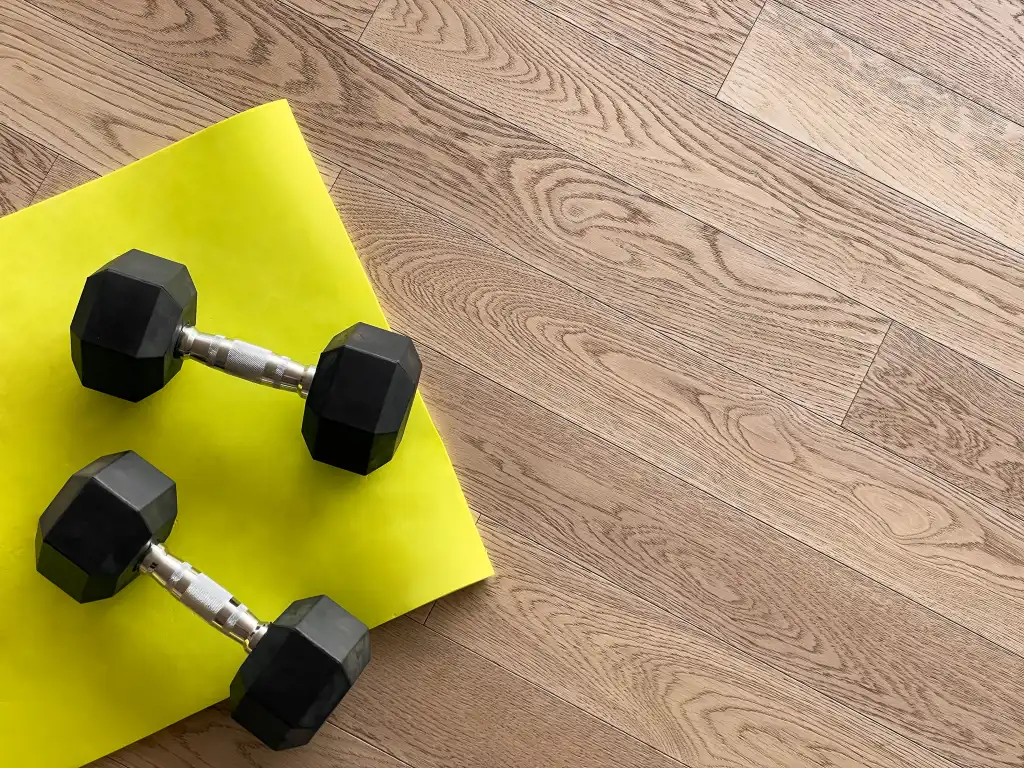 Two dumbbells on a yellow paper on a wooden floor.