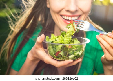 A young woman is eating a salad with a fork.
