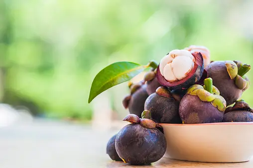 A bowl filled with fresh mangosteen fruit and a bottle of mangosteen extract.