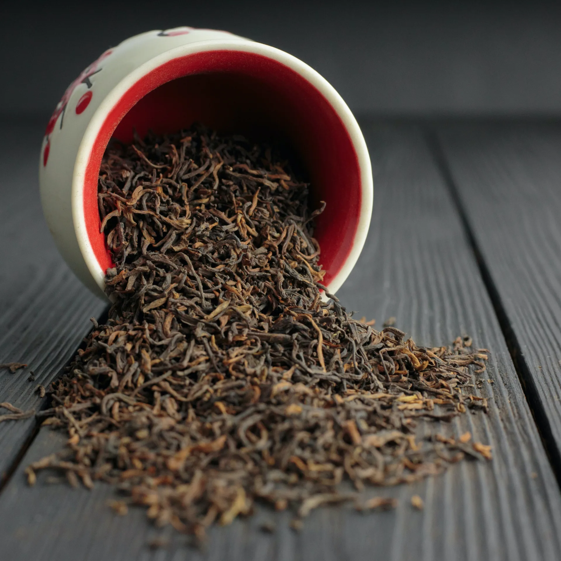 An overhead view of Black Tea Powder in a delicate bowl with scattered loose tea leaves around.