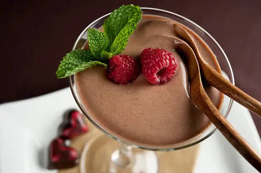 Decadent chocolate mousse adorned with raspberries and chocolate shavings.