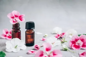 A glass bottle of geranium essential oil sits on a rustic wooden surface, bathed in soft natural light.