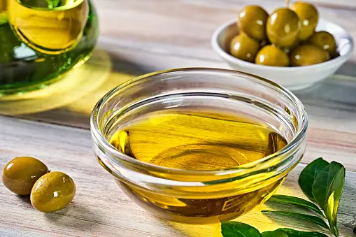 A bottle of extra virgin olive oil with fresh olives and a drizzling of oil