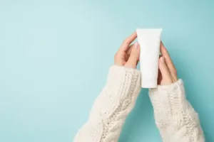 A woman's hands holding a tube of cream on a blue background.