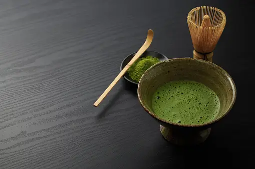 A cup of matcha with a wooden spoon next to it.