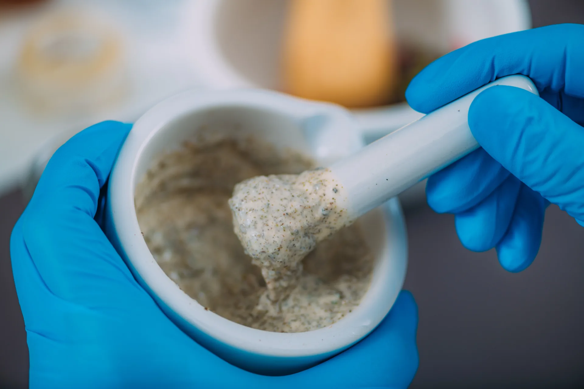 Gloved hands using mortar and pestle with paste.