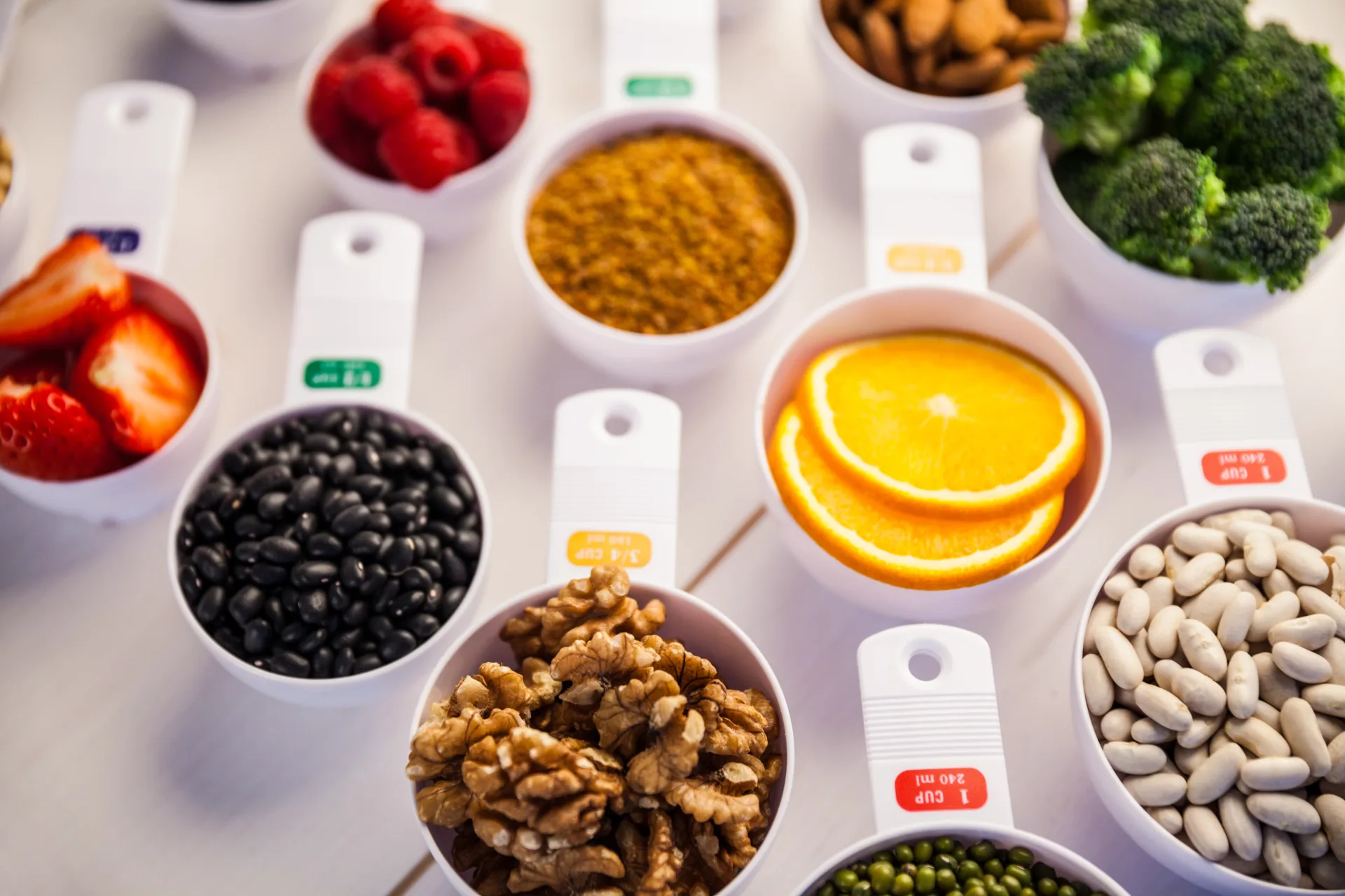 Measuring cups with assorted fruits, nuts, and vegetables.