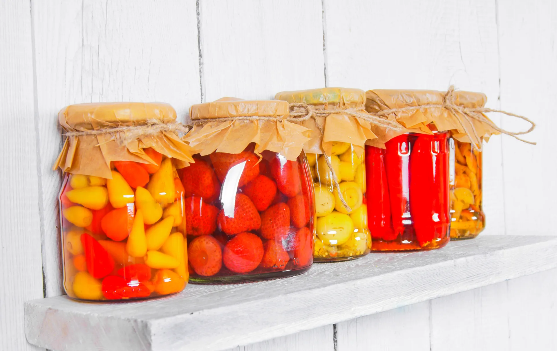 Assorted colorful pickled vegetables in jars on shelf.