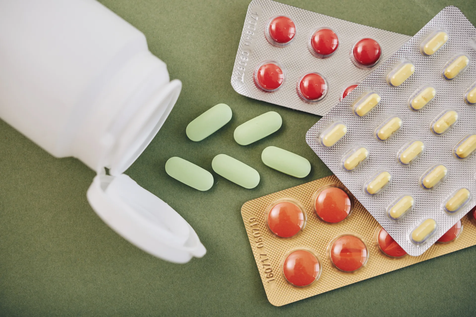 Various pills and blister packs on green background.