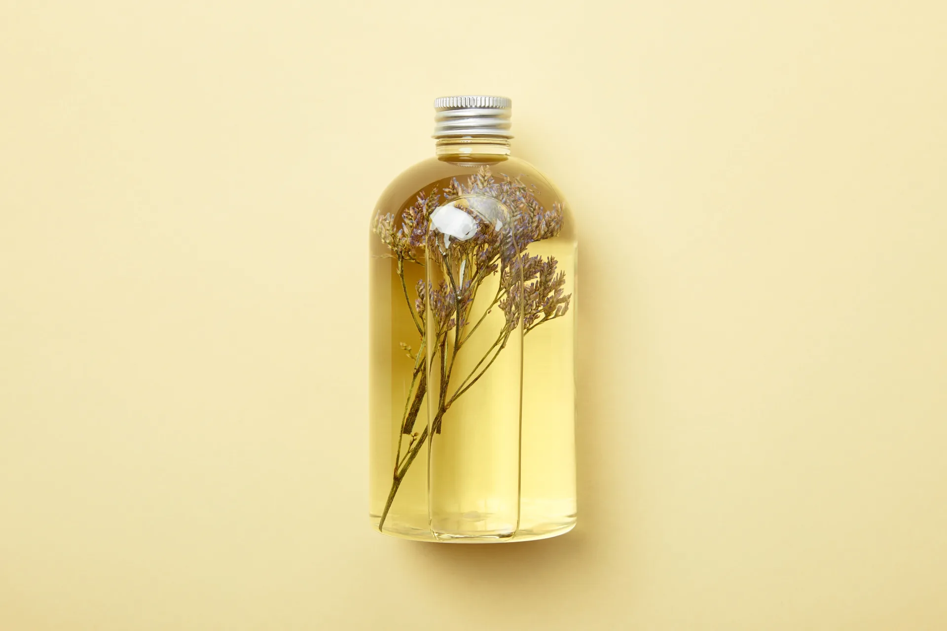 Glass bottle with flowers in oil, beige background.